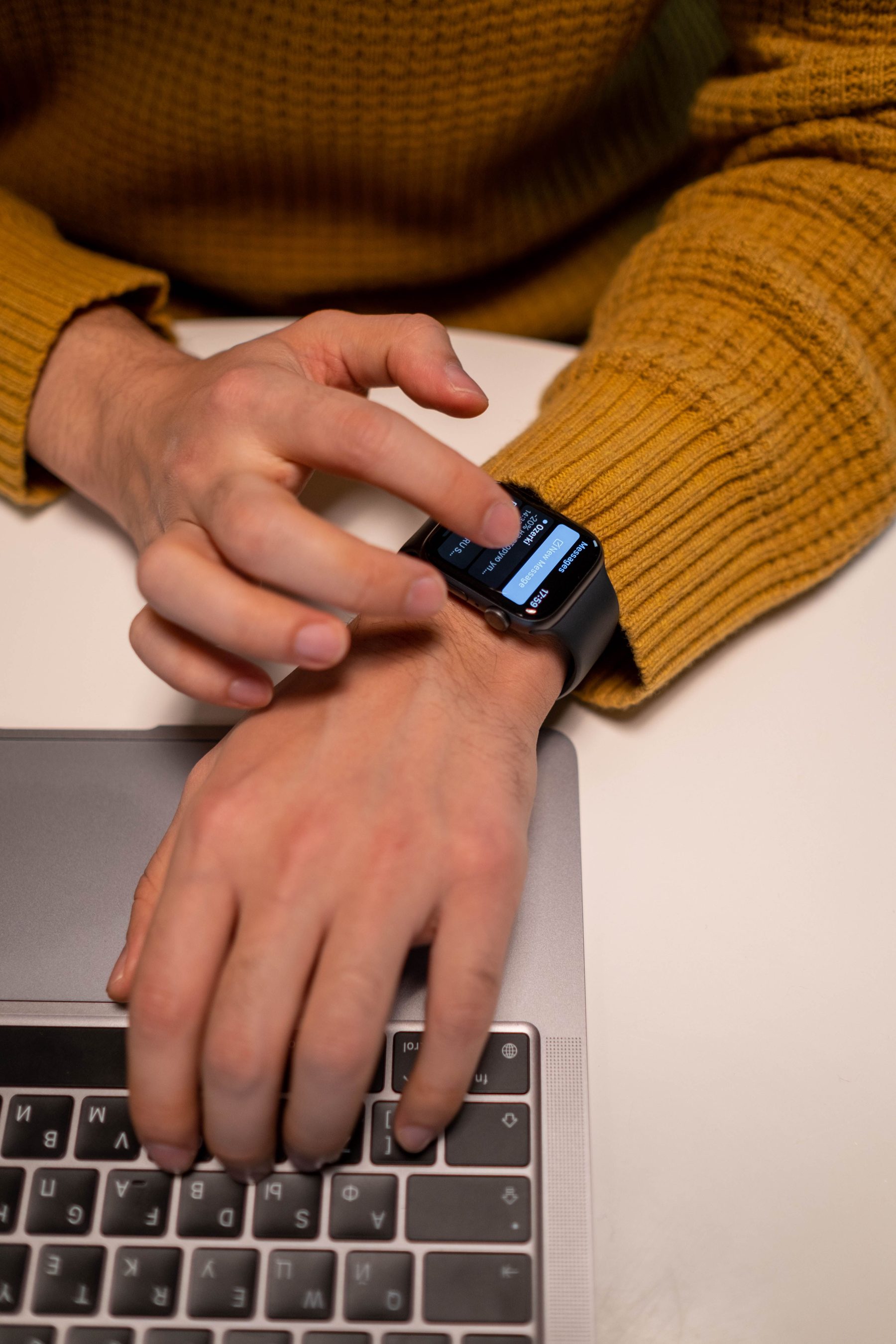 Person evaluating a smartwatch beside a laptop